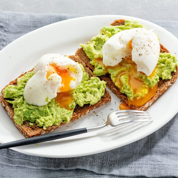 Two avocado toasts with runny poached eggs and black pepper on a white plate.
