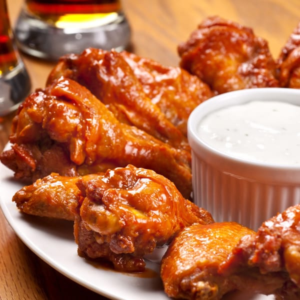 A plate of buffalo chicken wings with a side of ranch dressing and two glasses of beer.