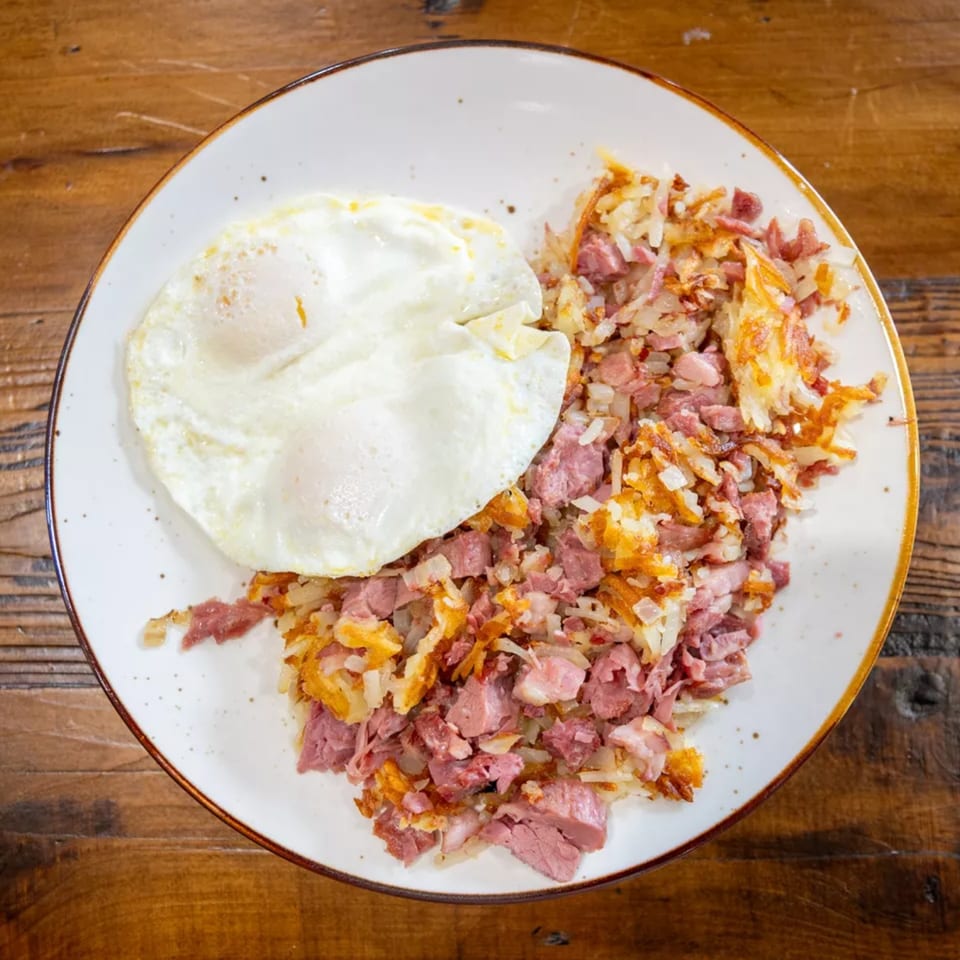 Plate of corned beef hash with crispy potatoes, onions, and a fried egg on a wooden table.